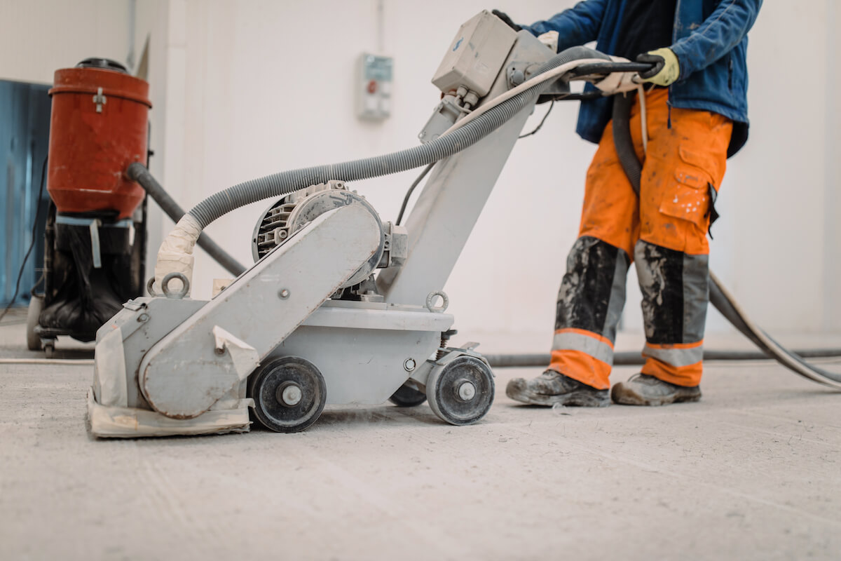 A worker operates a machine used to prepare the surface of a concrete factory floor prior to applying a floor coating.