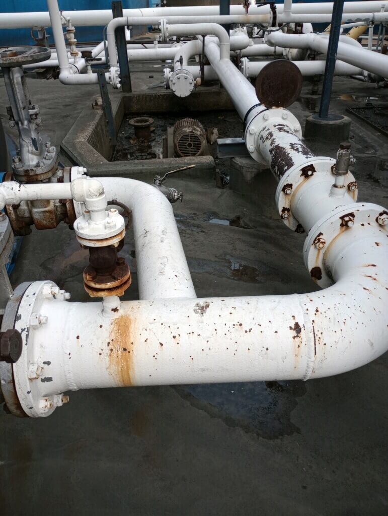 Rust is visible on the painted surface of steel piping at a liquid terminal.