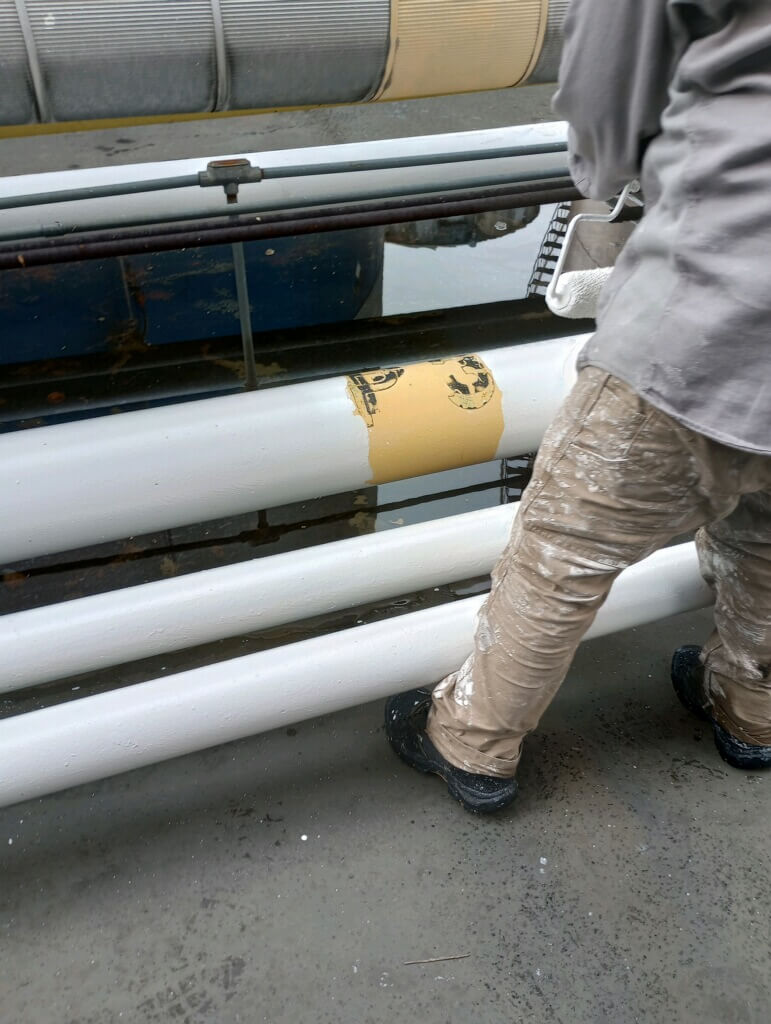 A painter coats over a patch of old yellow paint on a steel pipe at a liquid terminal.