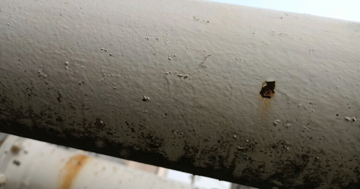 Dirt is visible on the underside of a coated steel pipe at a liquid terminal.