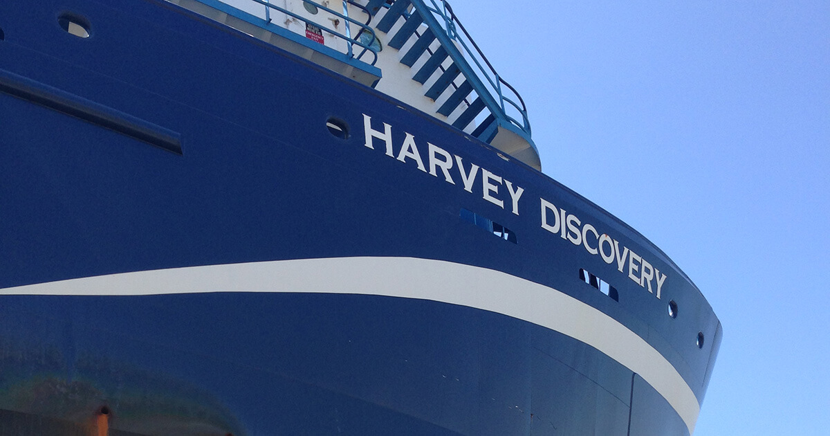 The blue hull and white lettering of the ocean supply vessel Harvey Discovery.