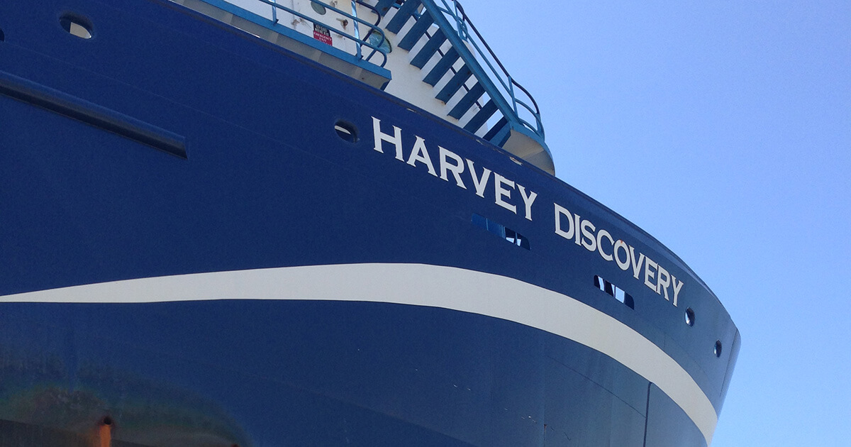 The blue hull and white lettering of the ocean supply vessel Harvey Discovery. 