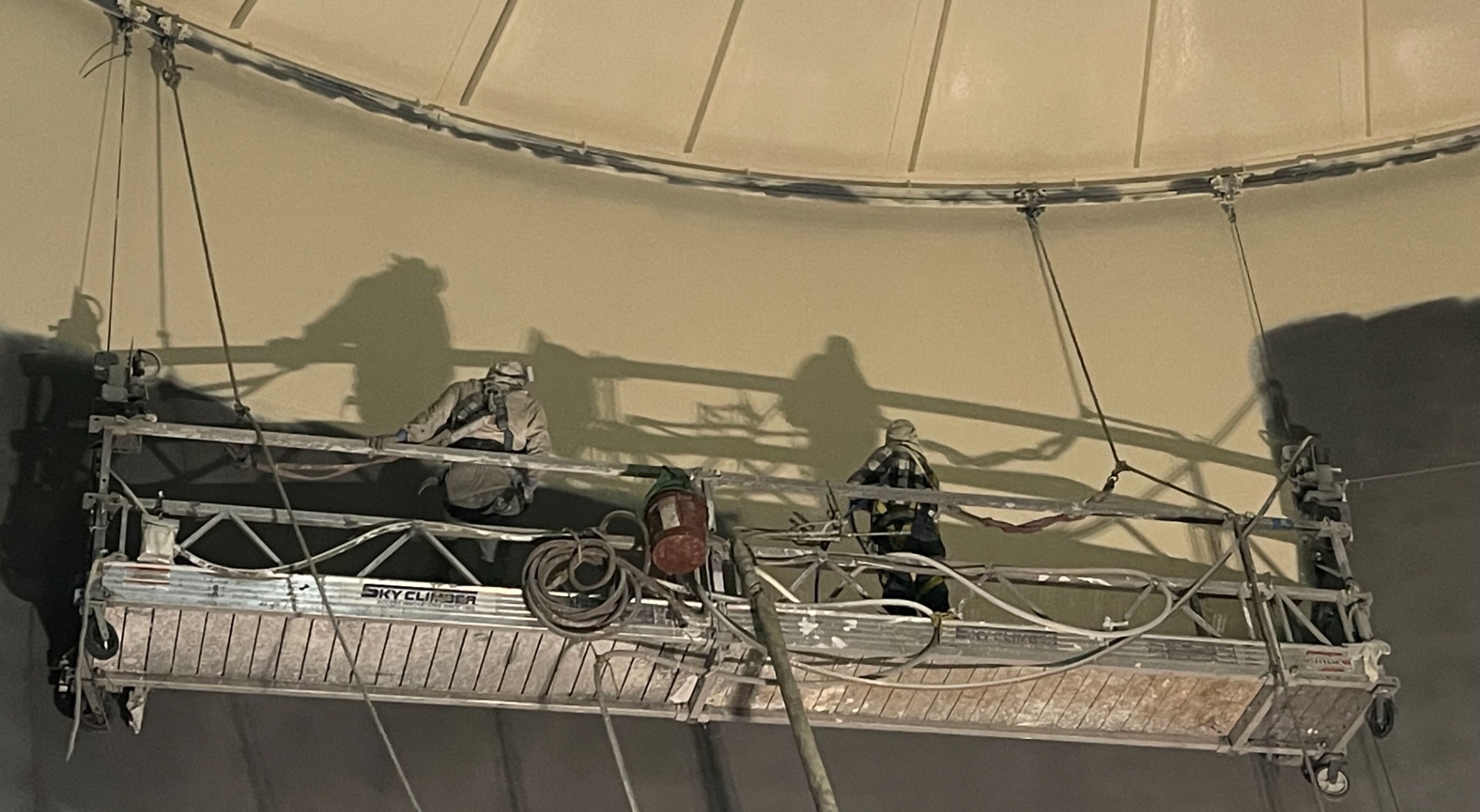 Two men standing on an elevated work lift applying paint to the interior surface of a potable water tank.