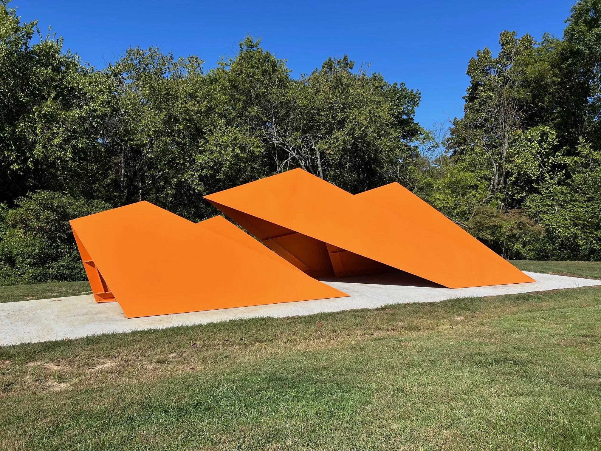 A wide-shot view of a large orange sculpture in an outdoor setting.